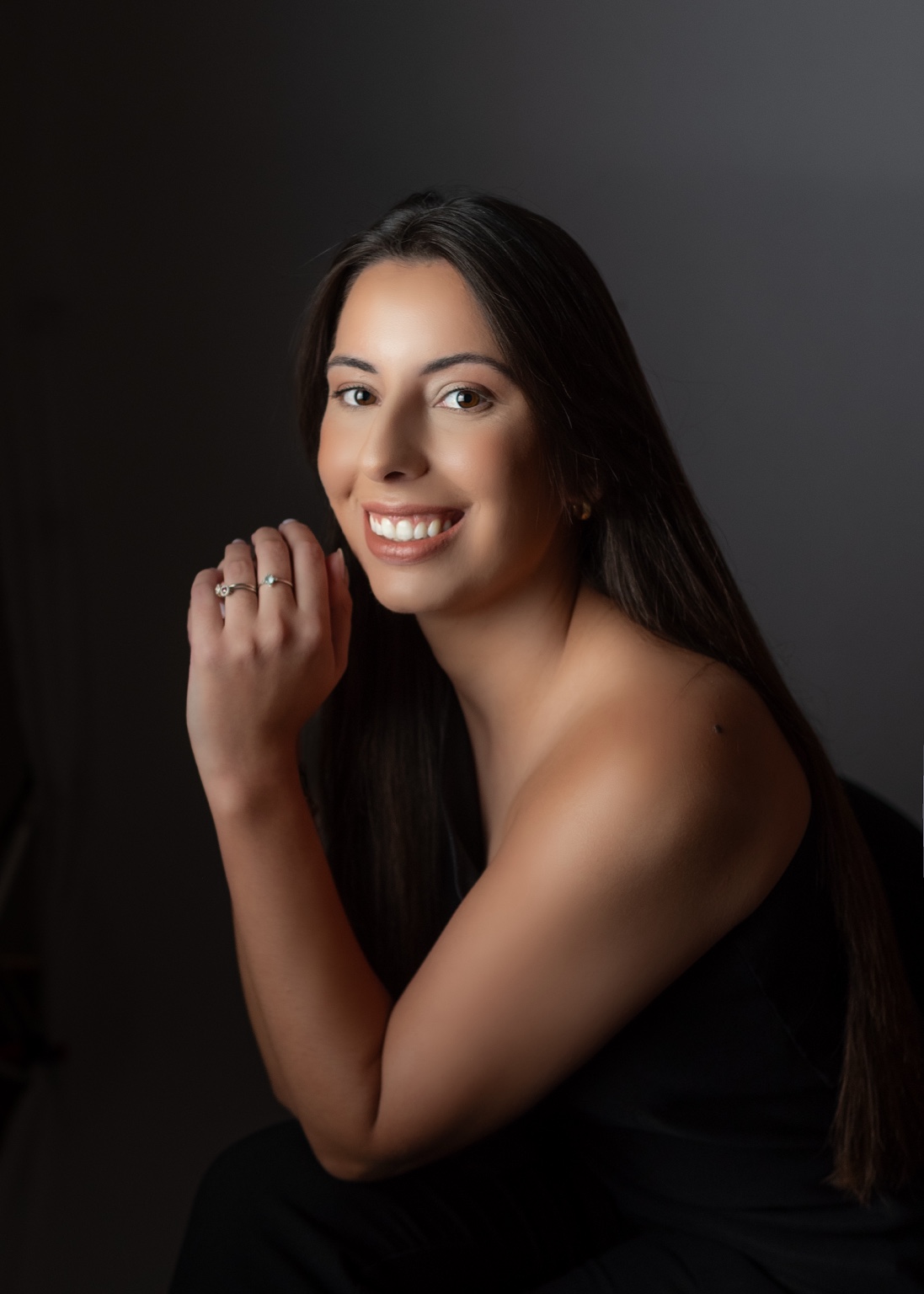 Gabriela Thereza Prado Bueno em retrato profissional, sorrindo, com a mão próxima ao rosto